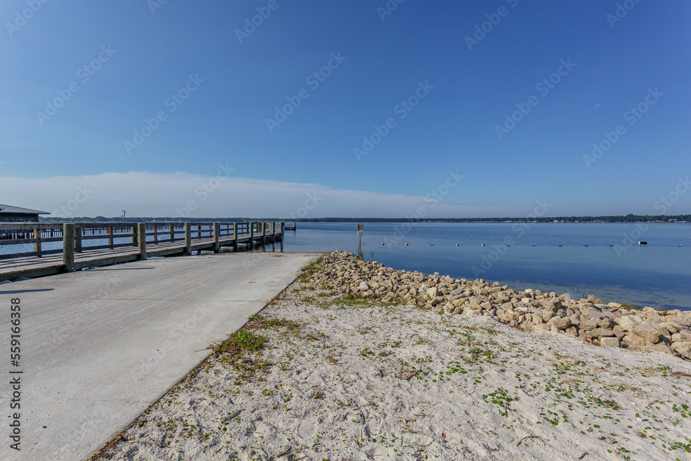 Sandy beach on a clear blue lake with palm trees and a long dock perfect for fishing