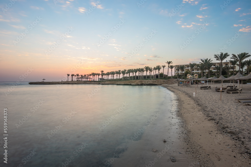 Palm trees on the seashore before dawn. Beautiful sunrise at sea. Dawn on the Red Sea. The sun is reflected in the sea. Palm trees against the background of the rising sun. Tropical sunrise