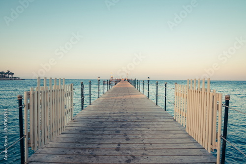 Wooden pier at sunrise in the tropical sea. Palm trees in the distance. Beautiful wooden pier. Long exposure of the sea as a haze