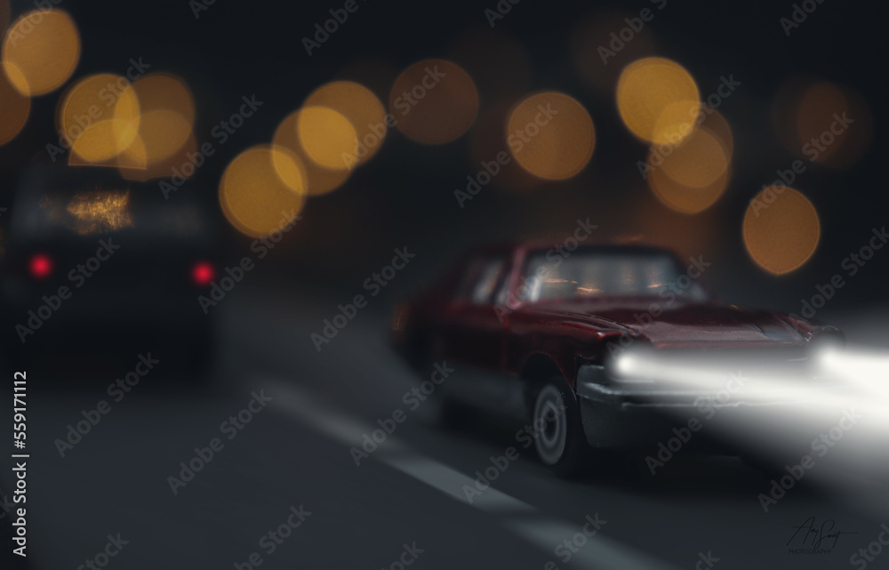 Retro car made into a nightime scene with headlights driving down the road.