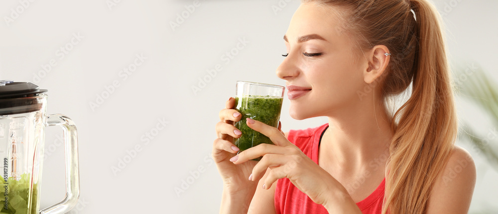 Fototapeta premium Pretty young woman drinking green smoothie at home