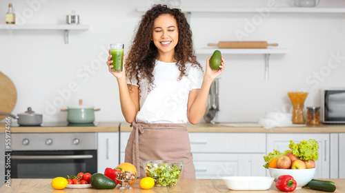 Happy African-American woman drinking healthy smoothie in kitchen