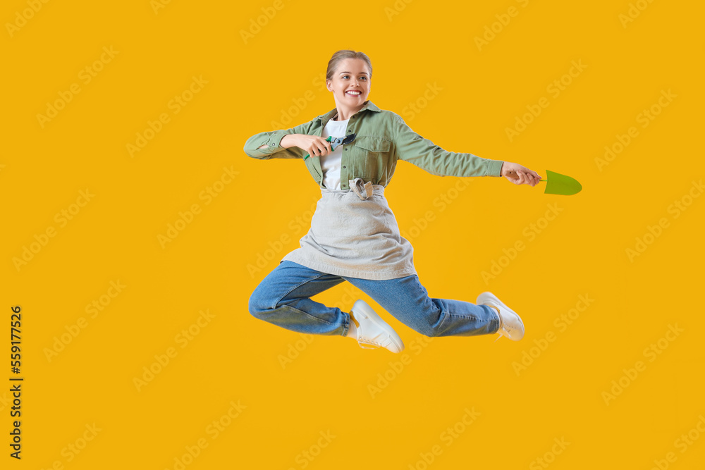 Female gardener with tools jumping on yellow background