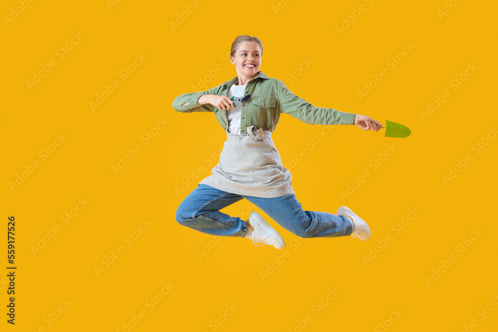 Female gardener with tools jumping on yellow background Female gardener with tools jumping on yellow background
