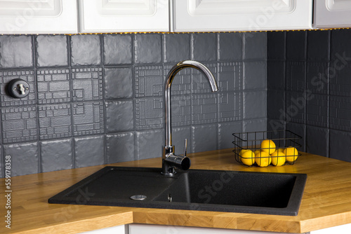 Quadro su tela Close up view of new modern kitchen solid wood butcher block oak counter with built in black rectangular granite sink, repainted gray color tile wall