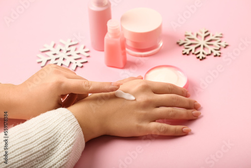 Woman applying cream onto her hand on pink background  closeup