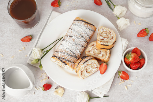 Plate with delicious sponge cake roll, fresh strawberries, floral decor and cup of coffee on light background