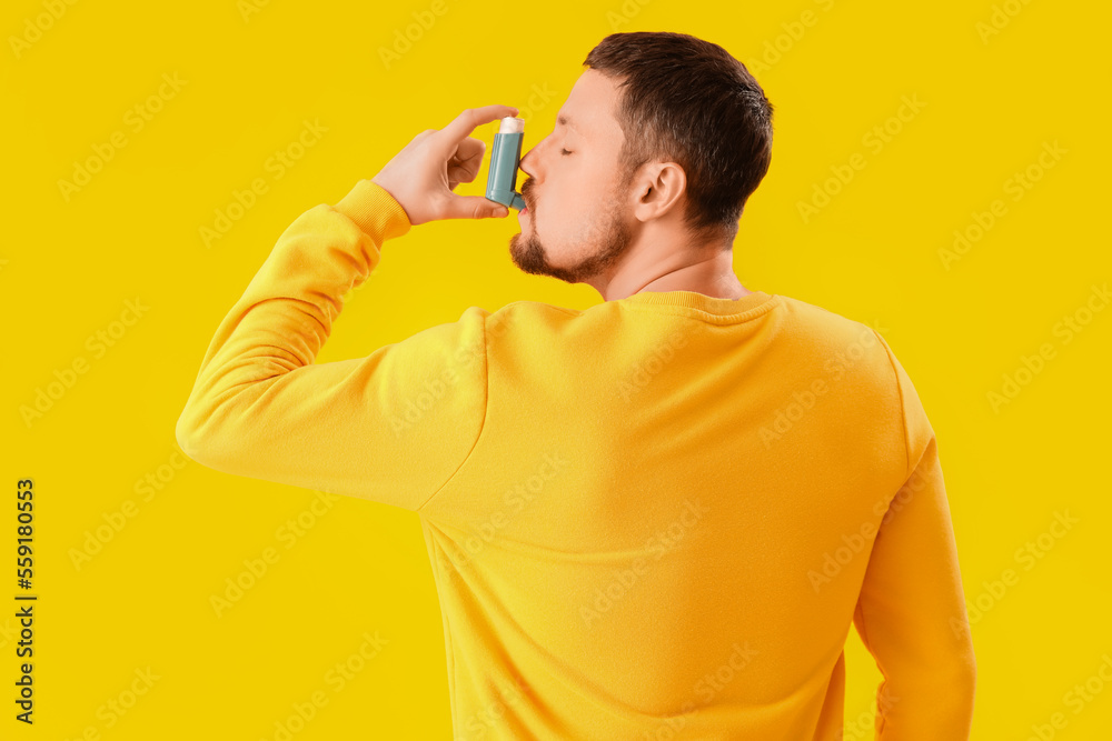 Sick man with inhaler on yellow background