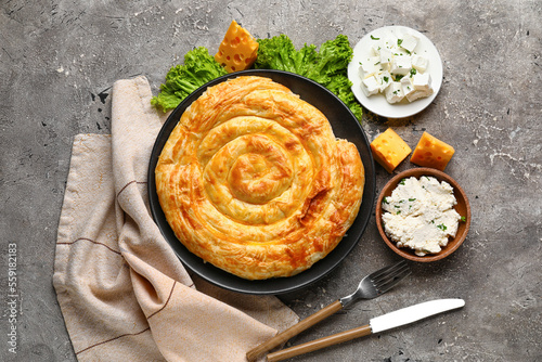 Plate with delicious cheese pie, lettuce and ingredients on grey table