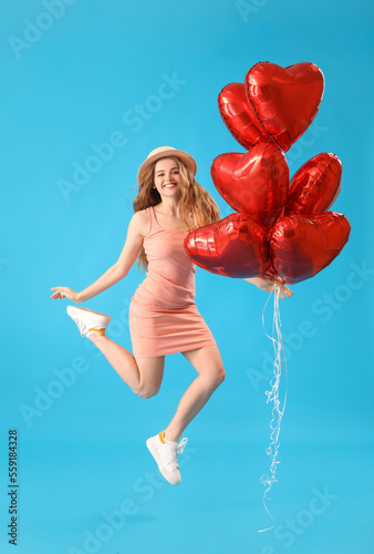 Happy jumping young woman with heart-shaped balloons on blue background. Valentine's Day celebration