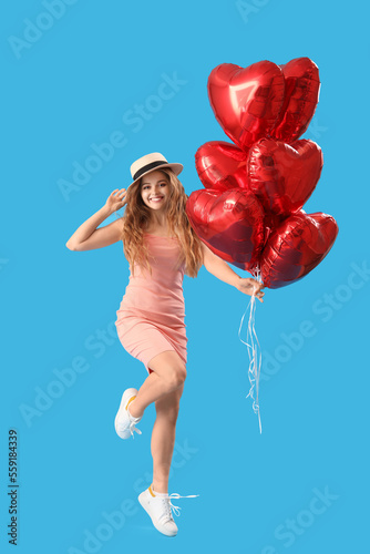 Beautiful young woman with heart-shaped balloons on blue background. Valentine's Day celebration