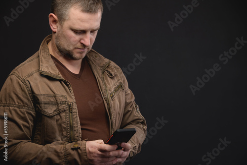 Portrait of a focused bearded man using his mobile phone, reading social media news, typing messages in stylish clothes, or focused on business matters