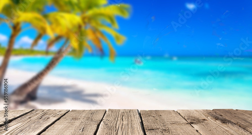 Beach summer background with wooden pier or table and landscape of beach with palms and blue sky. Free space