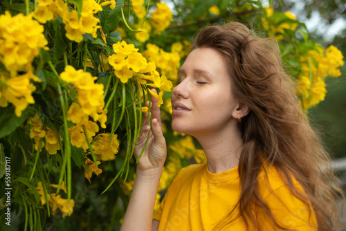 Portrait of happy beautiful bearded girl  young positive woman with beard is smelling beautiful yellow flowers in the garden  smiling  enjoying spring or summer day  breathing deep deeply fresh air