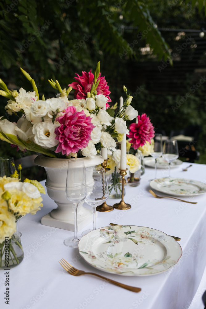 Flowers decorations on the table. Beautiful plates and candles.  Table setting by the pink, yellow. white flowers outdoor.