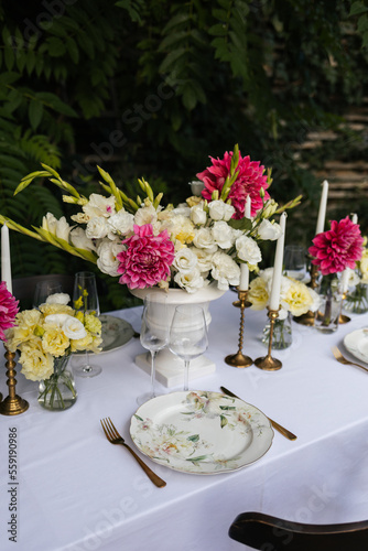 Flowers decorations on the table. Beautiful plates and candles. Table setting by the pink, yellow. white flowers outdoor.