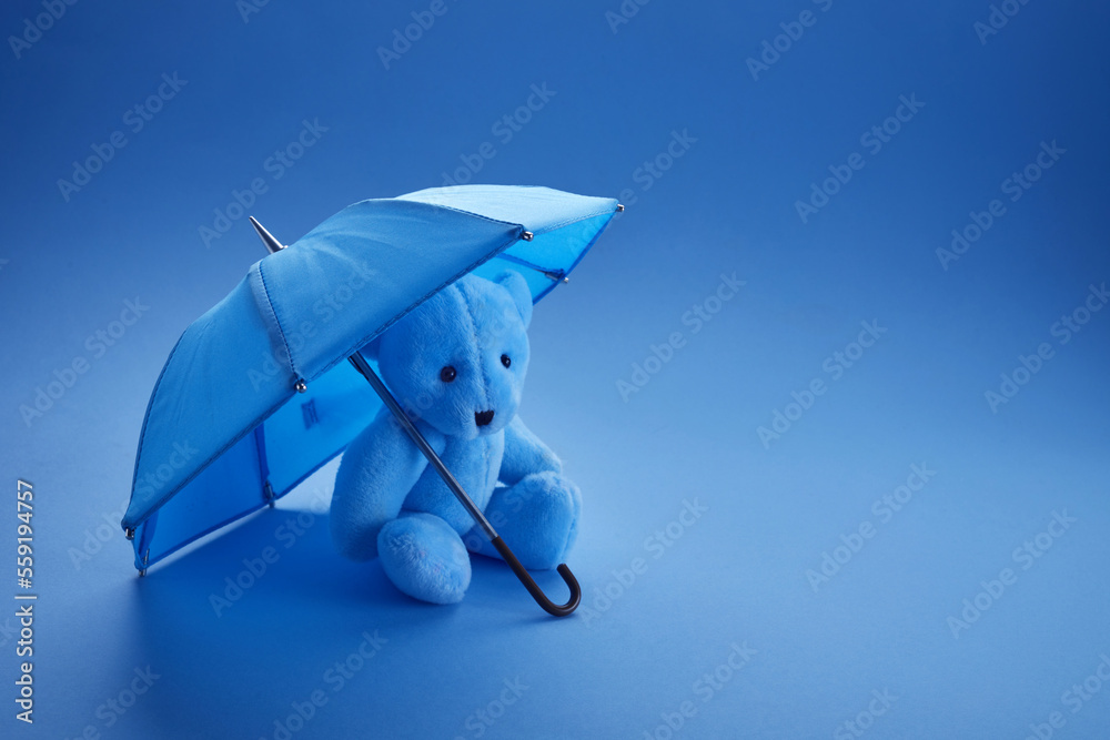Blue teddy bear with umbrella on blue background. Blue monday concept