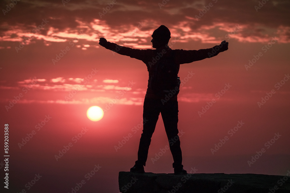 View of solo male person on a hill open arms and looking left on forground and sunrise at background