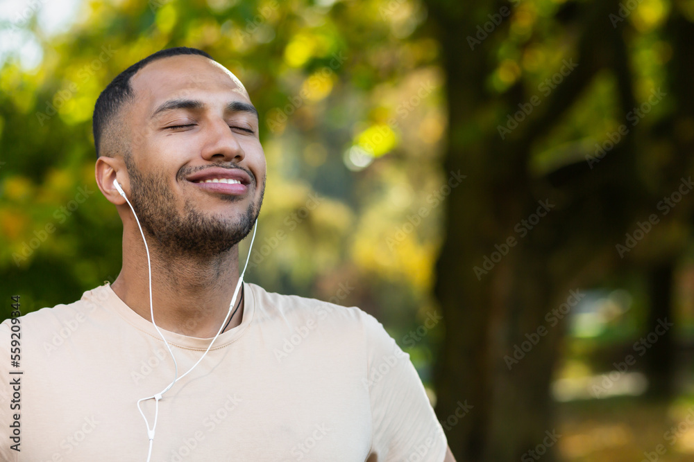 Close-up portrait of sportsman in park, hispanic man jogging in park with eyes closed breathing fresh air and resting, jogging with headphones listening to music and online radio and podcasts. Close-up portrait of sportsman in park, hispanic man jogging in park with eyes closed breathing fresh air and resting, jogging with headphones listening to music and online radio and podcasts.
