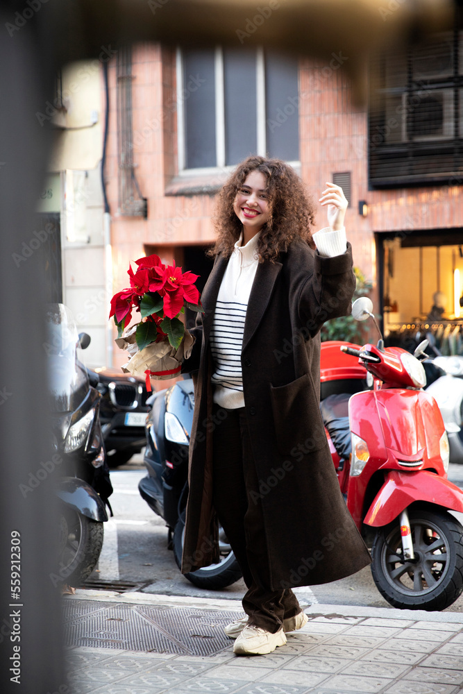 Model beautiful girl in a raincoat and sweater walks around the city with a flower