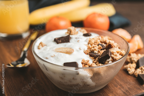 Granola cereal oatmeal with white yogurt, chocolate, banana fruit and nuts in a bowl on dark wooden board