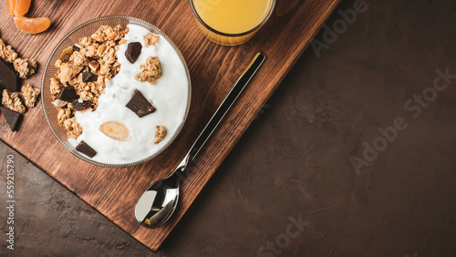 Granola cereal oatmeal with white yogurt, chocolate, fruist and nuts in a bowl on dark wooden board, top view photo