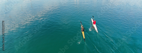 Aerial drone ultra wide slow shutter panoramic photo of athletes competing in sport canoe race in tropical lake with emerald waters