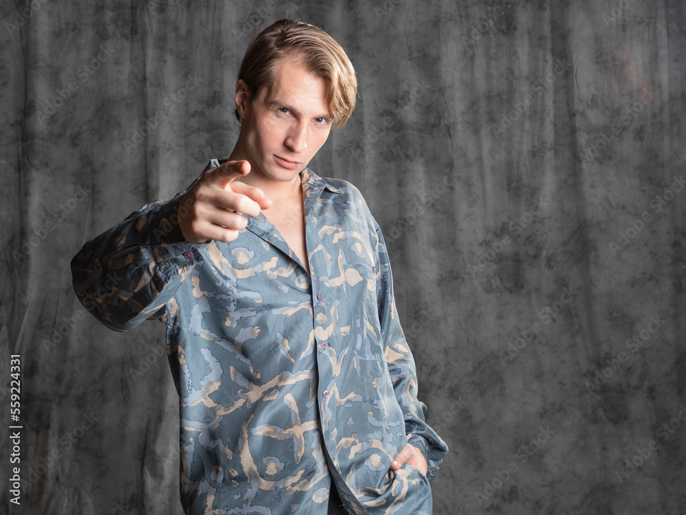 Stylish elegant young man in a blue silk shirt posing in the studio on a gray fabric background Stylish elegant young man in a blue silk shirt posing in the studio on a gray fabric background