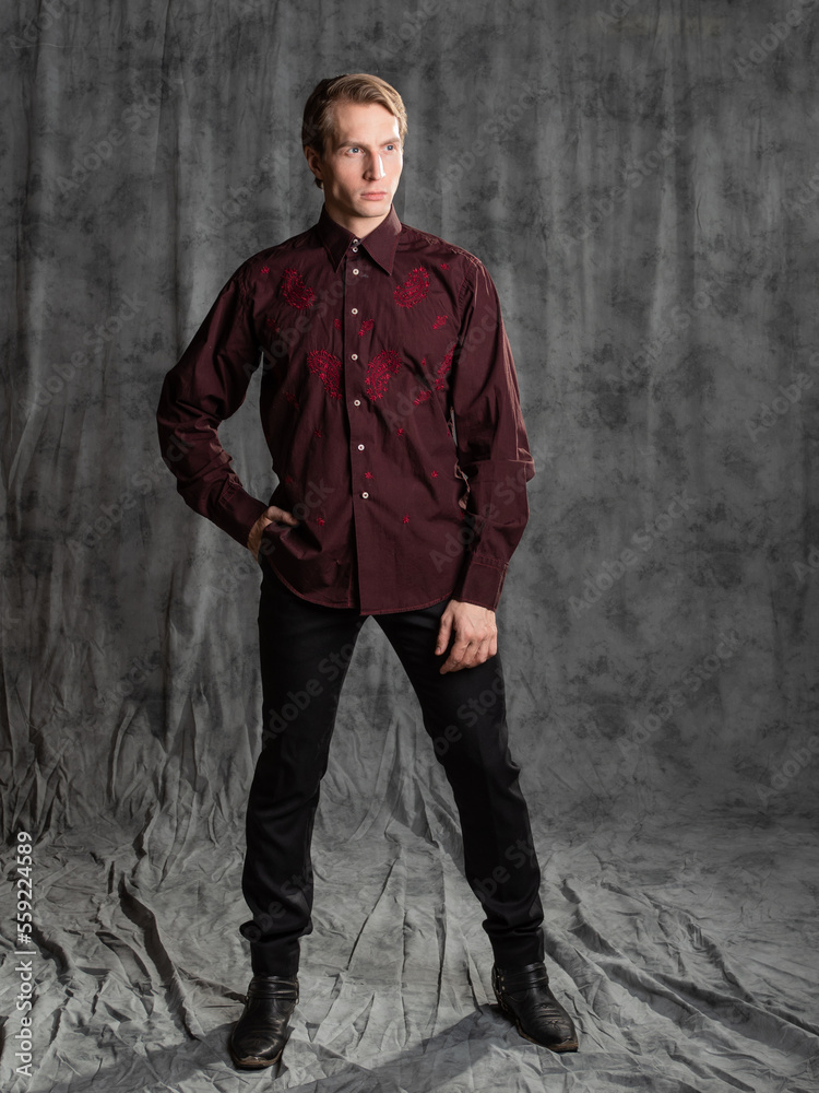 an attractive man in an elegant suit, burgundy shirt with embroidery. Photo in the studio on a gray background an attractive man in an elegant suit, burgundy shirt with embroidery. Photo in the studio on a gray background