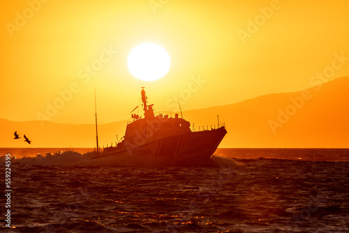Police boat goes fast across a bay in the sunset light with the Sun of the background © Evgeny Katyshev