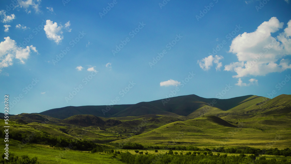 Beautiful minimalistic landscape, slope with lush green grass, blue sky with fluffy clouds, wallpaper