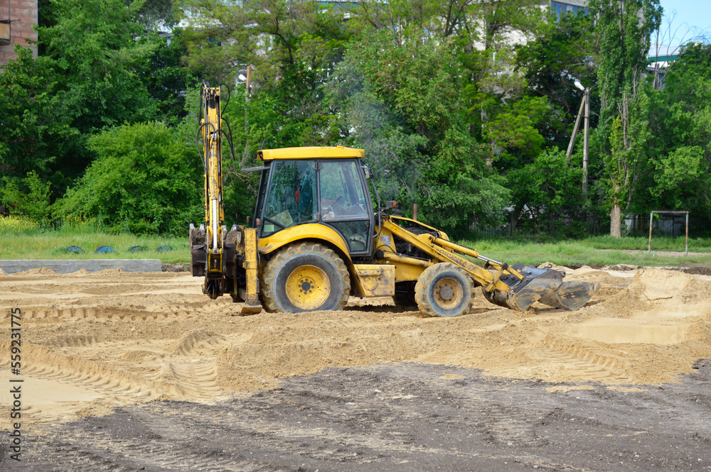 a yellow tractor with a blade and a bucket levels the sand at a construction site. Construction machinery does the hard work. soil preparation for the construction of a football field a yellow tractor with a blade and a bucket levels the sand at a construction site. Construction machinery does the hard work. soil preparation for the construction of a football field