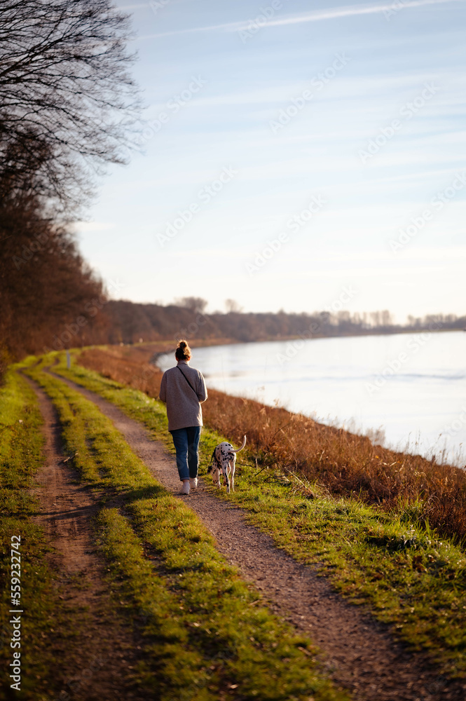 junge Frau geht mit Dalmatiner (Hund) an Fluss (Rhein) spazieren