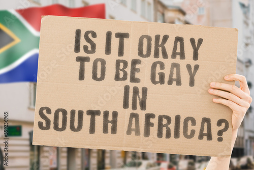 The question " Is it okay to be gay in South Africa? " is on a banner in men's hands with blurred background. Friendly. Passionate. Contact. Date. Dating. Lover. Partner. Boyfriend. Pleasant. Approval