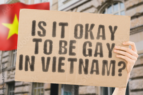 The question " Is it okay to be gay in Vietnam? " is on a banner in men's hands with blurred background. Friendly. Passionate. Contact. Date. Dating. Lover. Partner. Boyfriend. Pleasant. Approval