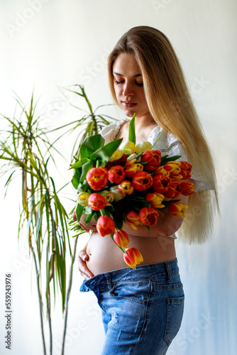 Fourth month of pregnancy. Beautiful pregnant woman with flowers. A series of photos of a pregnant girl. Concept of pregnancy, motherhood, mother's day.