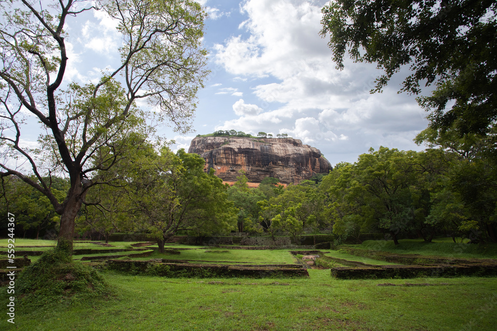 View to Sigiriya Sri Lanka. Path for tourists to climb the Lion Rock. Garden with trees around the sight seeing. Sky with clouds.
