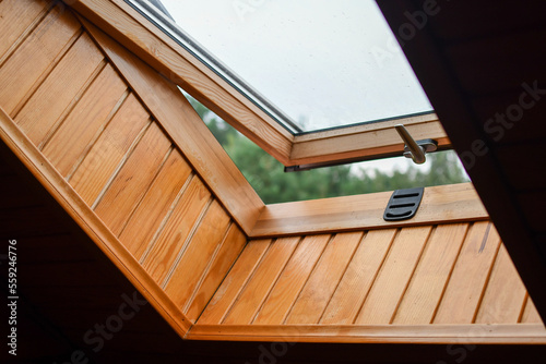 Detail of partially opened roof window installed into roof of the wooden log house