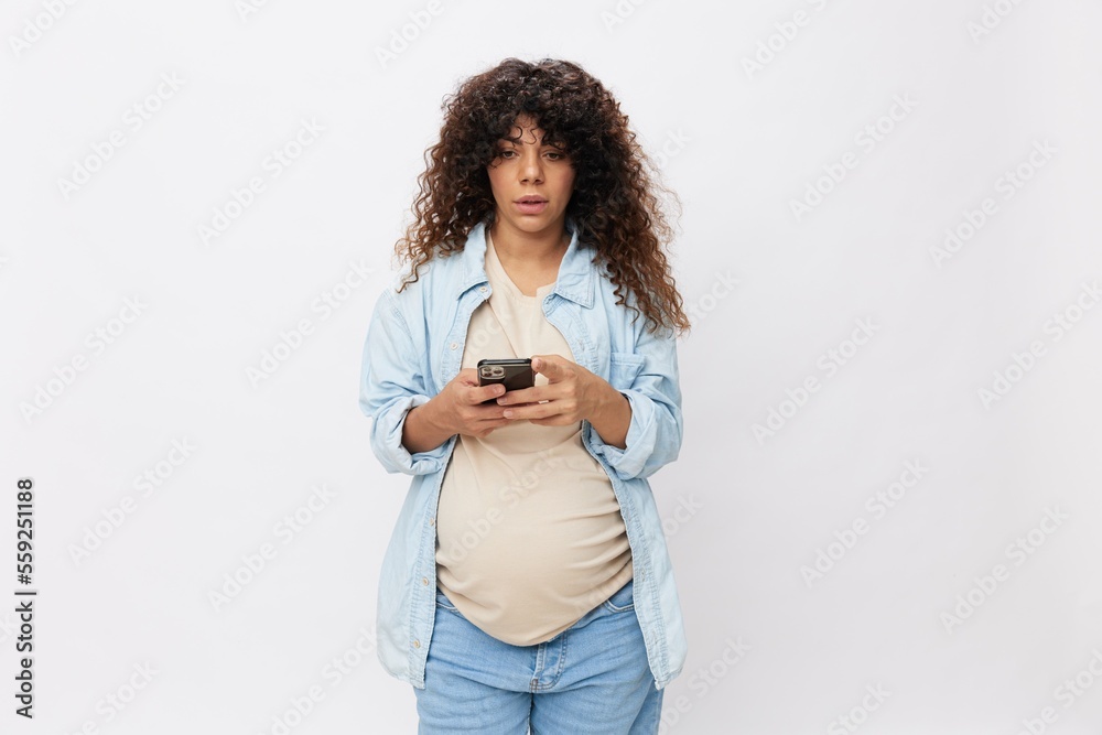 Pregnant woman pensive looking at phone in hand, online communication and correspondence, on white isolated background in t-shirt with blue shirt Pregnant woman pensive looking at phone in hand, online communication and correspondence, on white isolated background in t-shirt with blue shirt