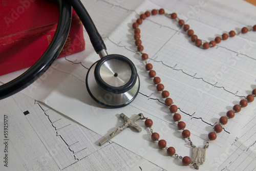 A stethoscope next to a crucifix over an electrocardiogram and a bible