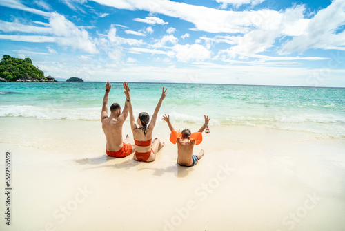 Fototapeta Naklejka Na Ścianę i Meble -  Photo of a happy family on tropical vacation, having fun on the tropical beach, playing with sea water. Little boy with parents.