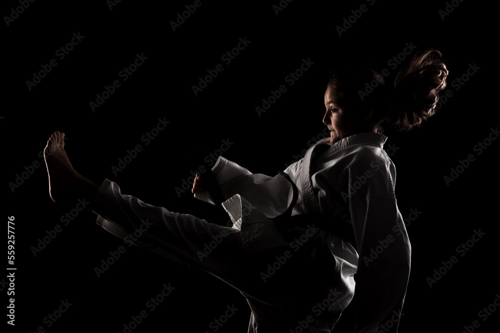 Young girl exercising karate. Child in kimono against black background.