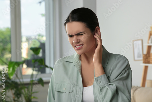 Young woman suffering from ear pain at home photo