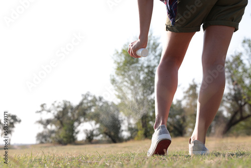 Woman applying insect repellent onto leg in park, closeup. Space for text