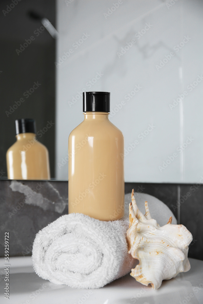 Bottle of shower gel and rolled towel with shell on sink in bathroom Bottle of shower gel and rolled towel with shell on sink in bathroom