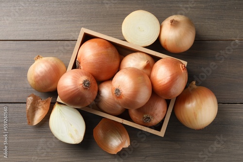 Whole and cut onions on wooden table, flat lay