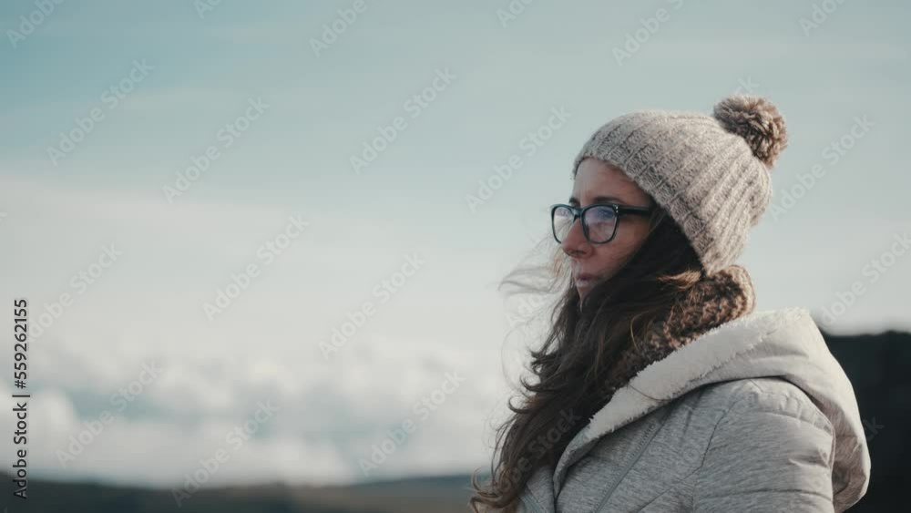 Slow motion close-up of a thoughtful inspired woman enjoying the beauty of nature in the mountains. Young, millennial, and wearing glasses, a gray jacket, hat, and scarf. Travel and adventure visuals. Slow motion close-up of a thoughtful inspired woman enjoying the beauty of nature in the mountains. Young, millennial, and wearing glasses, a gray jacket, hat, and scarf. Travel and adventure visuals.
