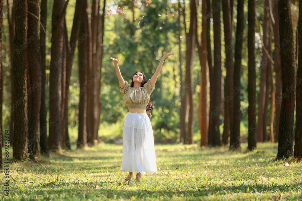 beautiful woman stand and throwing rose petals happy play on her vacation relax in the pine tree park at morning natural light, happily and freedom concept beautiful woman stand and throwing rose petals happy play on her vacation relax in the pine tree park at morning natural light, happily and freedom concept