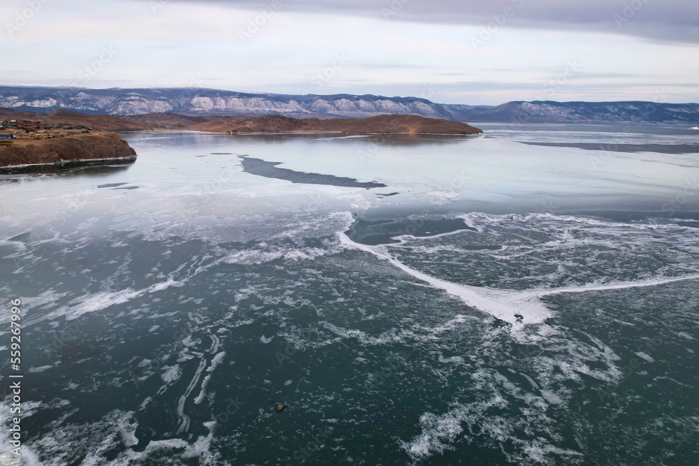 Frozen Lake Baikal, aerial view. Cloudy stormy sky, clear ice in the cracks. Winter landscape.
