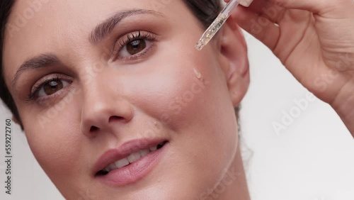 Caucasian woman using pipette with serum and smiling. Skincare and face treatment with natural components. Closeup portrait of beautiful female face with brown eyes. Girl using face oil with pipette.